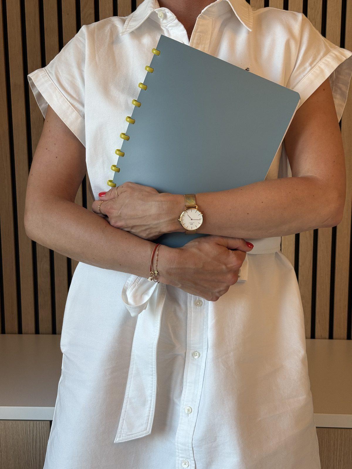Stéphanie tenant un carnet d’organisation contre elle, montre et bracelets dorés au poignet