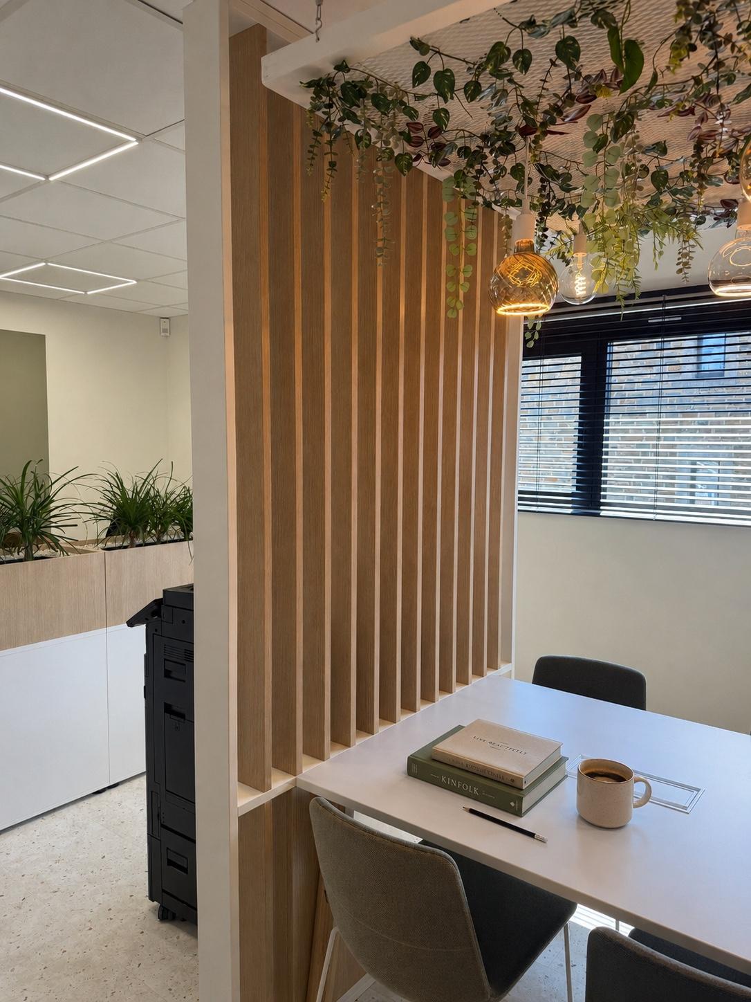 Espace de réunion lumineux : table avec livres et tasse de café, claustra en bois clair et plantes suspendues